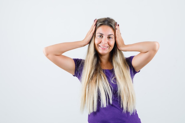 Young lady holding hands to head in violet t-shirt and looking pretty , front view.