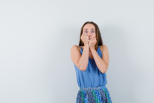 Young lady holding hands on her cheeks in blouse,skirt and looking scared , front view. space for text