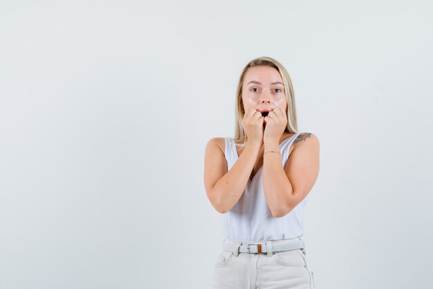 Young lady holding hands on her dropped jaw in white blouse and looking emotional free space for your text