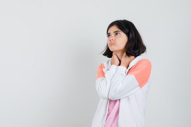 Young lady holding hands on her neck in jacket, pink shirt and looking thoughtful.