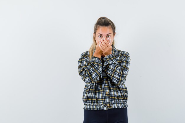 Young lady holding hands on mouth in shirt, shorts and looking surprised , front view.