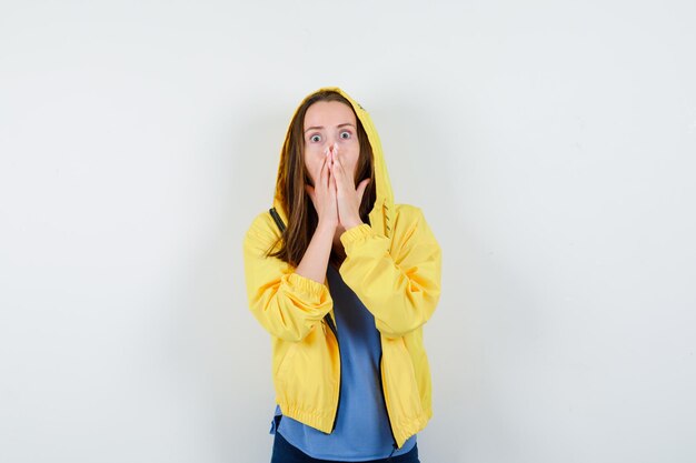 Young lady holding hands on mouth in t-shirt, jacket and looking scared