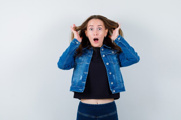 Young lady holding hands near head in blouse and looking amazed. front view.