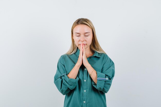 Young lady holding hands in praying gesture in green shirt and looking peaceful.