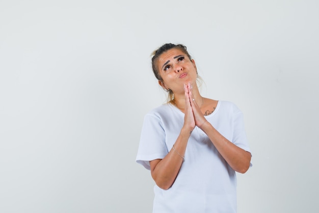 Young lady holding hands in praying gesture in t-shirt and looking hopeful 