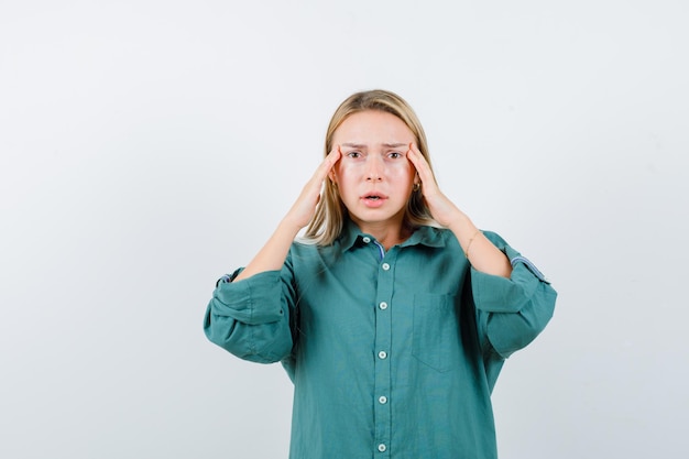 Free photo young lady holding hands on temples in green shirt and looking depressed.