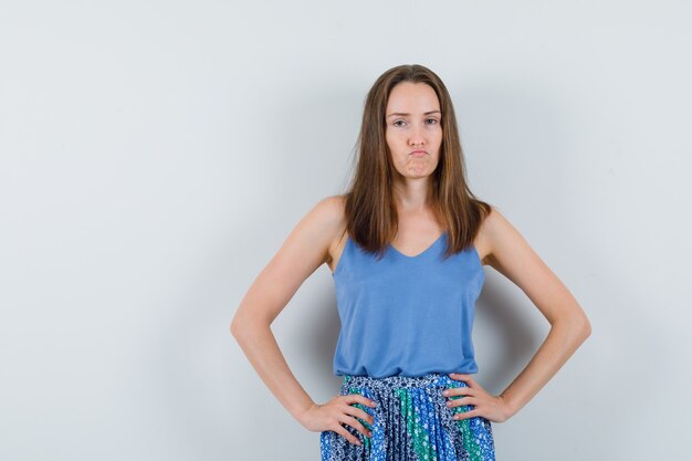 Young lady holding hands on waist in singlet, skirt and looking pensive