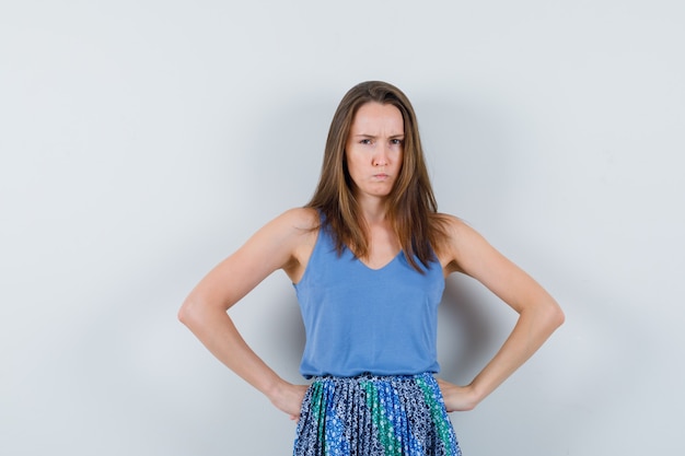 Free photo young lady holding hands on waist in singlet, skirt and looking spiteful