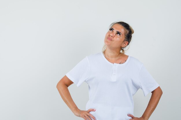 Young lady holding hands on waist in t-shirt and looking focused  