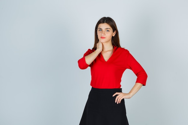 Young lady holding one hand on neck, another hand on hip in red blouse