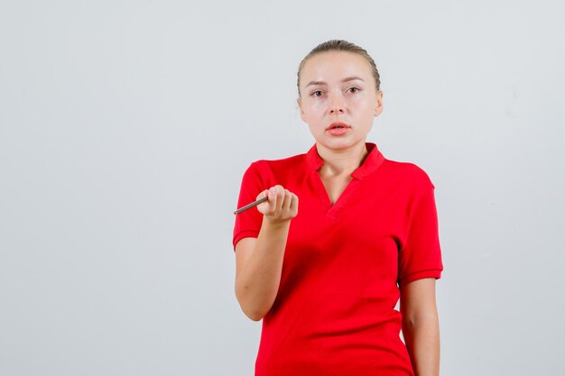 赤いTシャツに鉛筆を持って困惑している若い女性