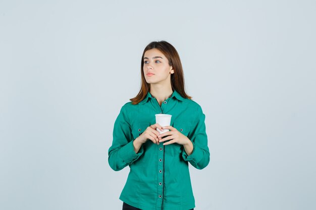 Молодая дама держит пластиковую чашку кофе в рубашке и смотрит задумчиво. передний план.