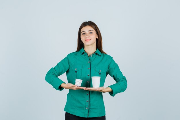 Young lady holding plastic cups of coffee in shirt and looking pleased , front view.