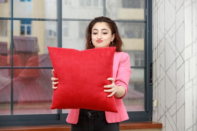 Free photo young lady holding red pillow and looking at it