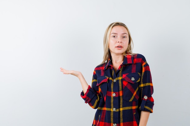 Young lady holding something in checked shirt and looking charming. front view.