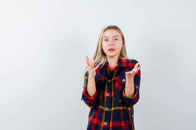Free photo young lady holding something in checked shirt and looking puzzled , front view.