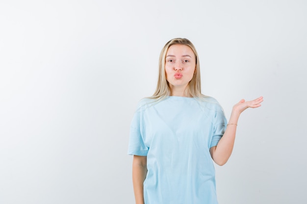 Young lady holding something while pouting lips in t-shirt and looking pretty , front view.