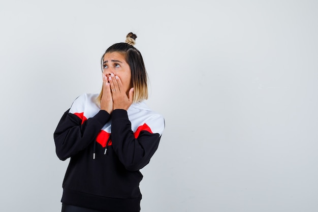 Young lady in hoodie sweater holding hands on mouth and looking puzzled