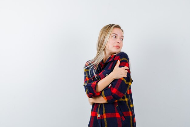 Young lady hugging herself in checked shirt and looking cute. front view.