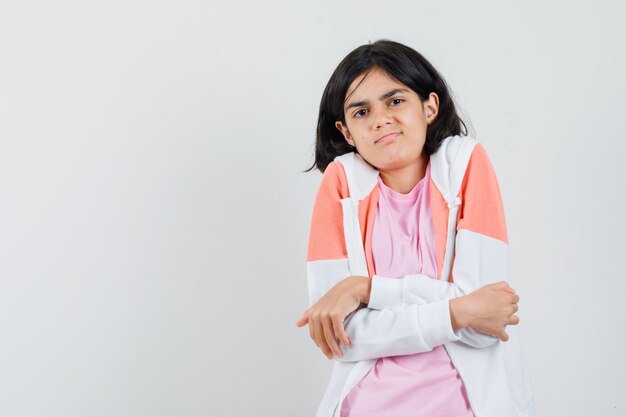 Young lady hugging herself in jacket, pink shirt and looking chilly.