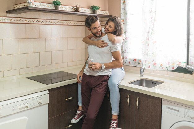 Giovane donna che abbraccia uomo con la tazza in cucina