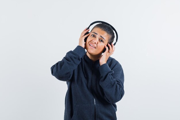 Young lady in jacket holding hands on earphones 