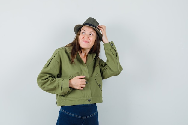 Foto gratuita giovane donna in giacca pantaloni cappello grattandosi la testa e guardando smemorato