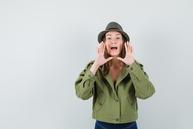 Free photo young lady in jacket pants hat shouting or announcing something