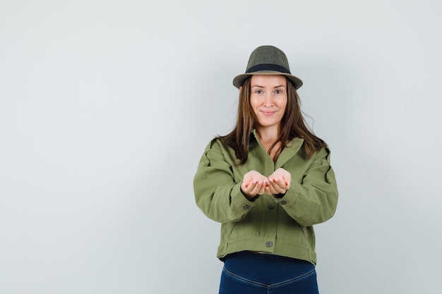 Young lady in jacket pants hat stretching cupped hands and looking gentle  