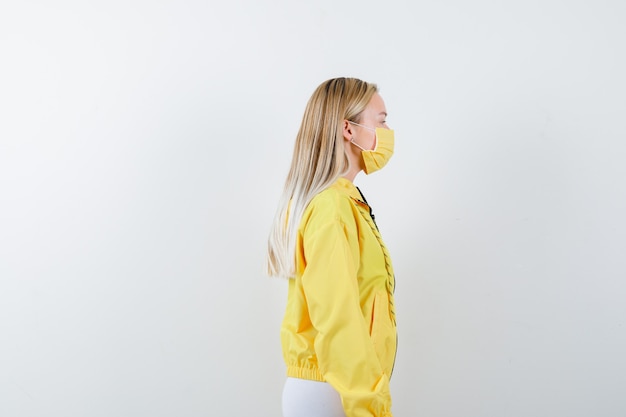 Young lady in jacket, pants, mask looking at the front of her and looking pensive .