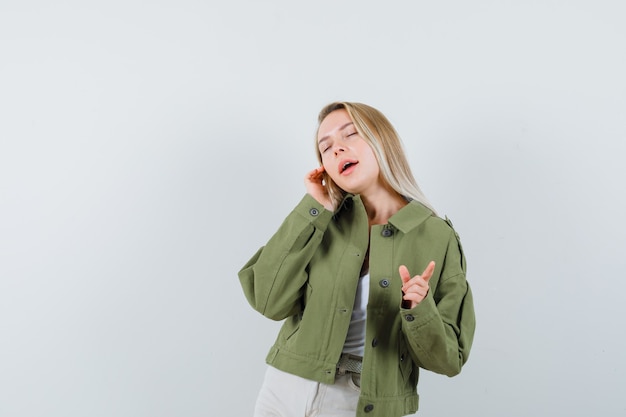 Young lady in jacket, pants pointing away and looking delighted , front view.