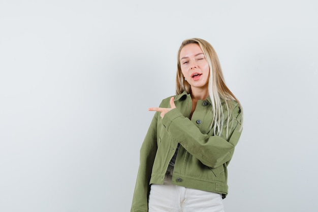 Young lady in jacket, pants pointing to the left side and looking confident , front view.