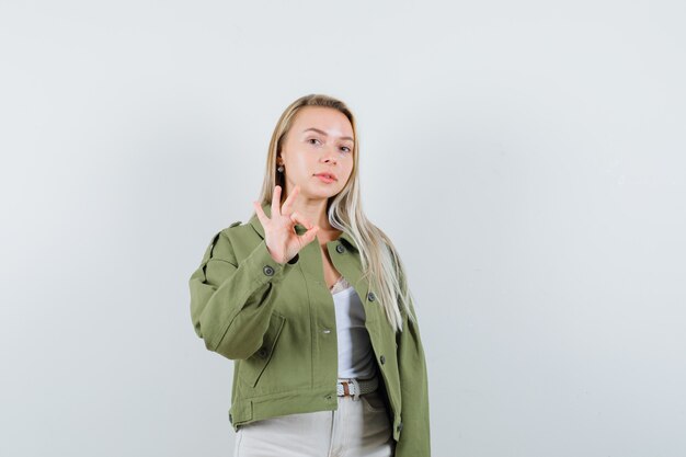 Young lady in jacket, pants showing ok gesture and looking confident , front view.