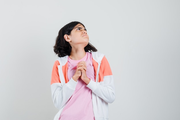 Young lady in jacket, pink shirt combining her hands while looking aside and looking hopeful