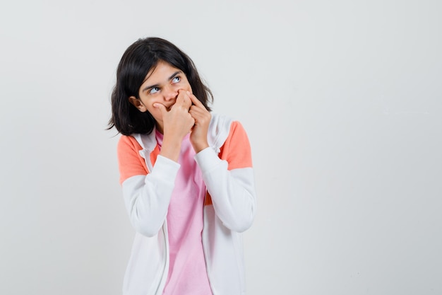 Giovane donna in giacca, camicia rosa che punta la guancia e sembra turbata