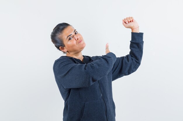 Young lady in jacket pointing to her arm and looking powerful 