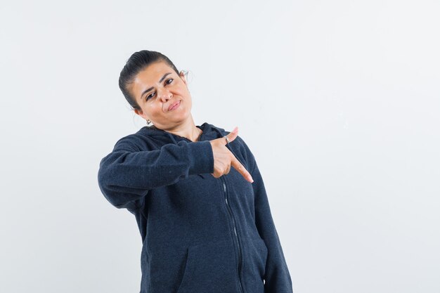 Young lady in jacket pointing at left corner and looking serious 