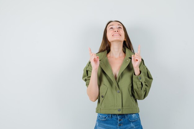 Young lady in jacket shorts pointing fingers up and looking grateful  