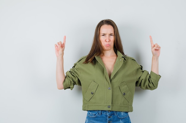 Free photo young lady in jacket shorts pointing up while scowling