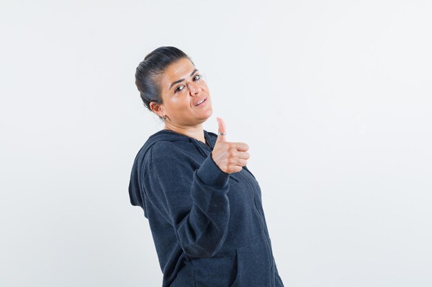 Young lady in jacket showing thumb up and looking assured 