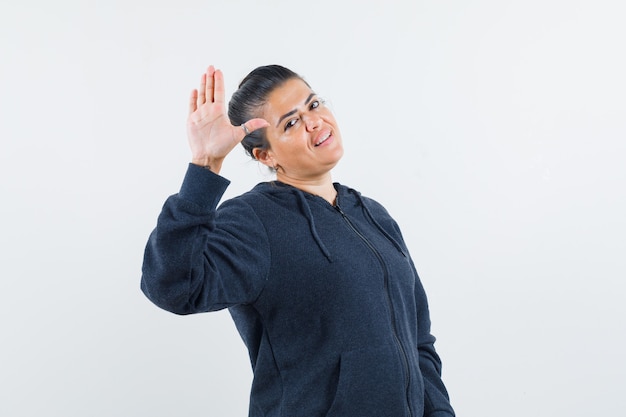 Young lady in jacket waving hand for goodbye and looking confident 