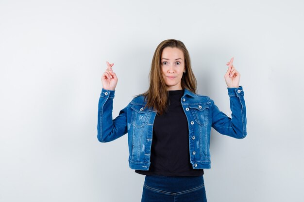 Young lady keeping fingers crossed in blouse and looking hopeful. front view.