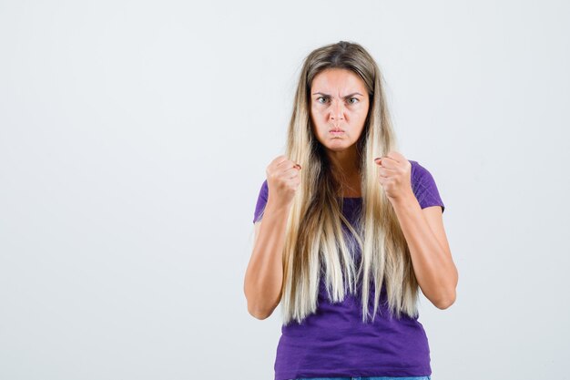 Young lady keeping fists clenched in violet t-shirt and looking spiteful , front view.