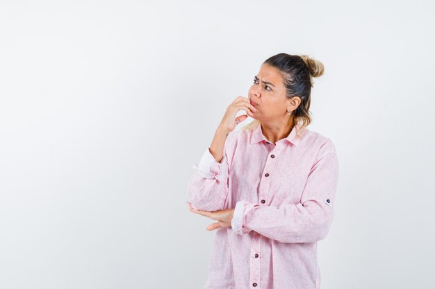 Young lady keeping hand on chin in pink shirt and looking thoughtful