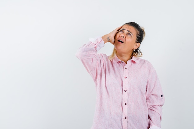 Young lady keeping hand on head in pink shirt and looking mournful 