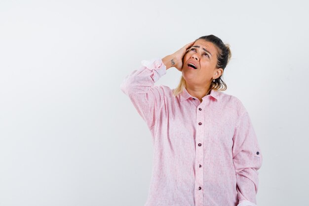 Young lady keeping hand on head in pink shirt and looking mournful 