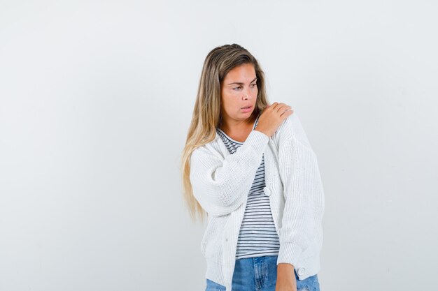 Young lady keeping hand on shoulder in t-shirt, jacket and looking pensive , front view.