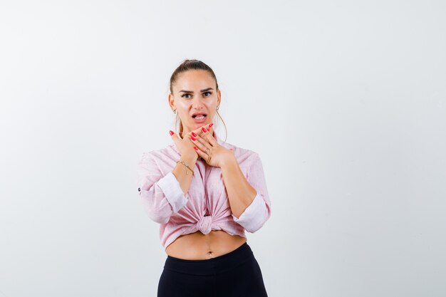 Young lady keeping hands on chin in shirt, pants and looking surprised , front view.