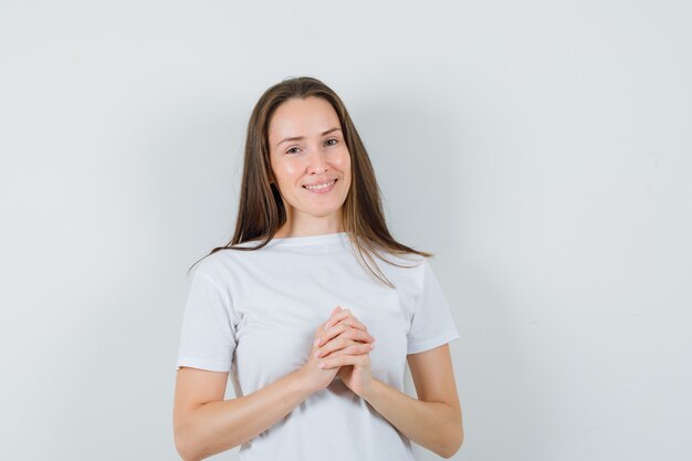 Young lady keeping hands clasped in white t-shirt and looking beautiful 