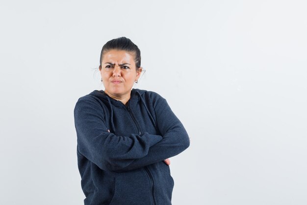 Young lady keeping hands crossed while souring her face in jacket and looking offended. front view. space for text